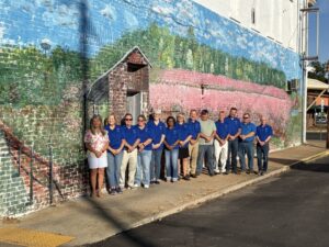New welcoming mural adorns historic building in downtown Johnston, SC. Pictured from left is Beth Clark, mural artist, and Johnston Development Corp. Board members Chair Gaye Holmes, Vice Chair Frank Davis, Treasurer Donna Livingston, Secretary Bridget Clark, Leigh Hillary, Debra Aston, Billy Miller, David Herlong, Ricky Deese, Chris Whatley, Don Smoak, and Dean Campbell. Not pictured are Mary Anne Hair, Shane Massey, Noah Peterson, and Ann Yonce.